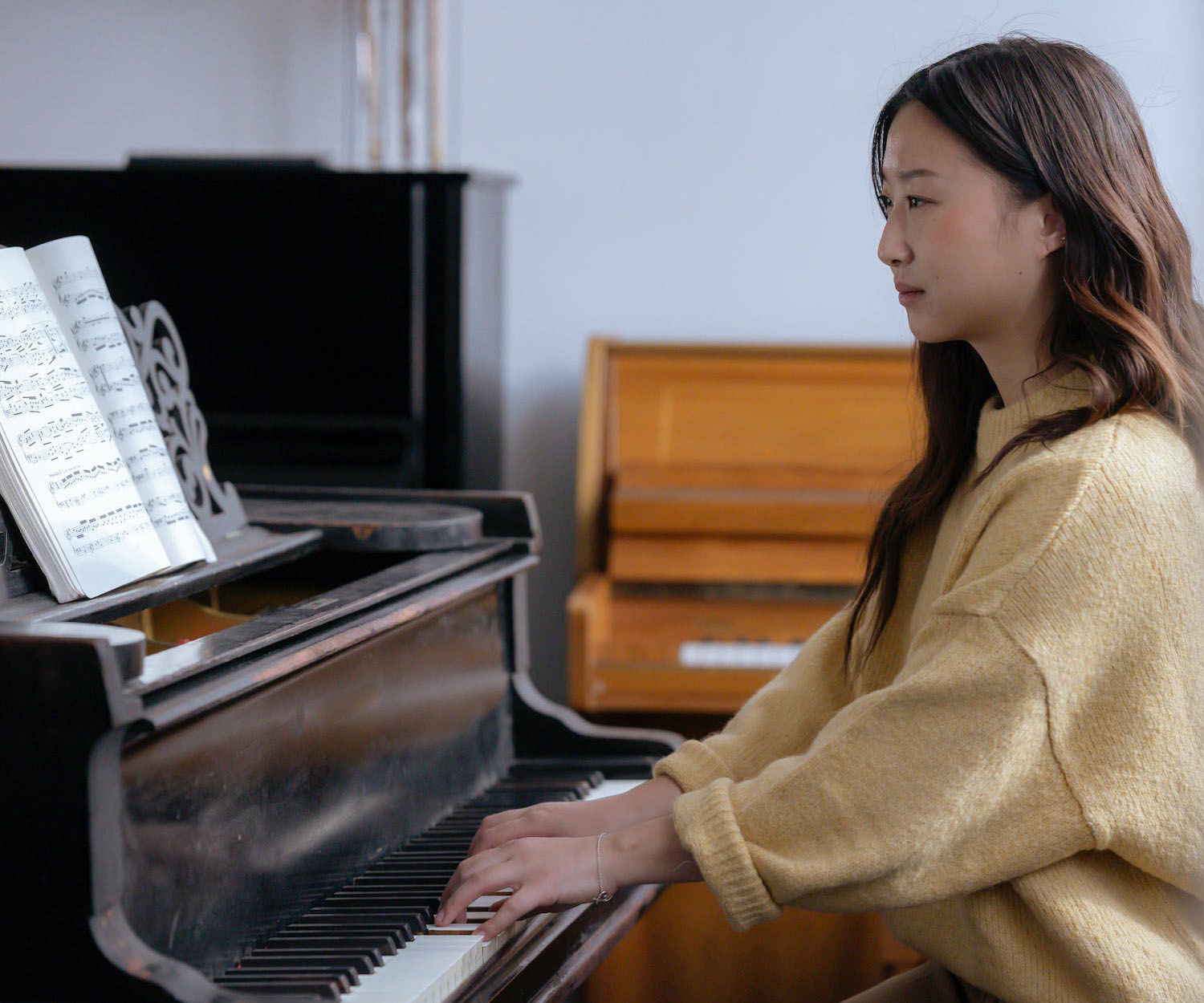 Side view of Asian woman in casual clothes practicing music on piano while sitting in bright classroom